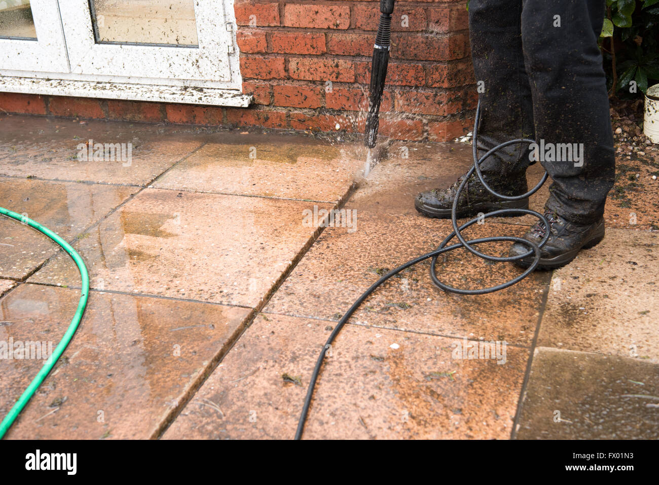 Middle-aged white man jet-washing his garden patio near his white plastic conservatory getting ready for summer in his English garden Stock Photo
