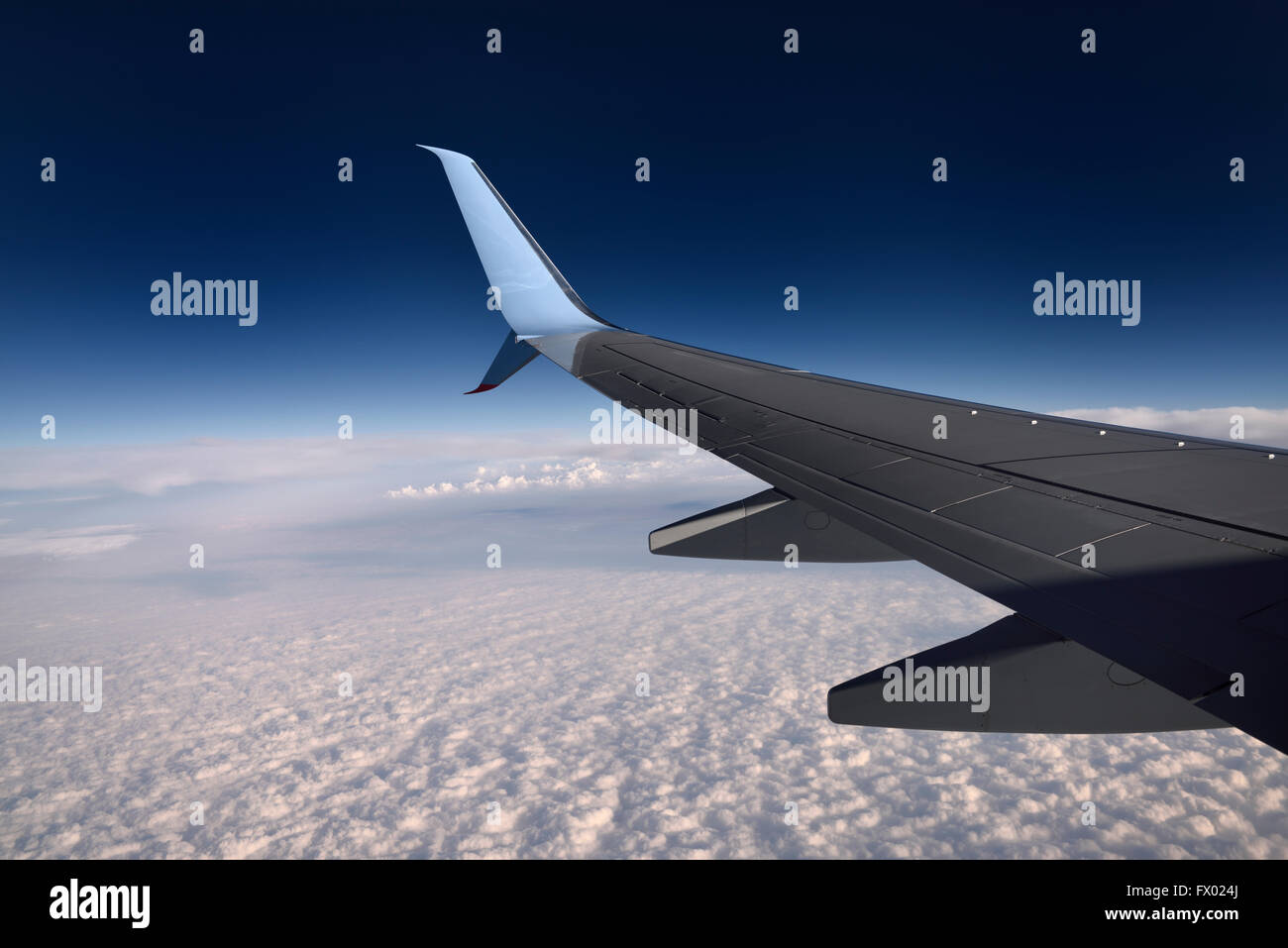 Jet aircraft wing flying above clouds with blue sky Stock Photo