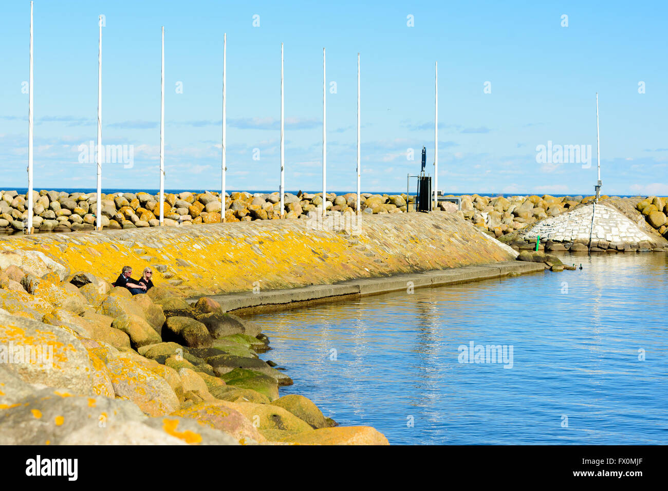 Simrishamn, Sweden - April 1, 2016: Two persons sit down by the stone pier and enjoy the warm sunshine on this fine spring day. Stock Photo