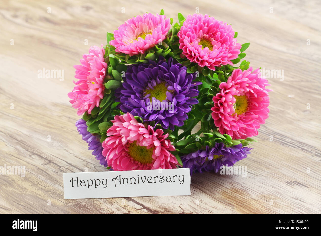 Happy Anniversary card with colorful daisy bouquet on wooden surface Stock Photo
