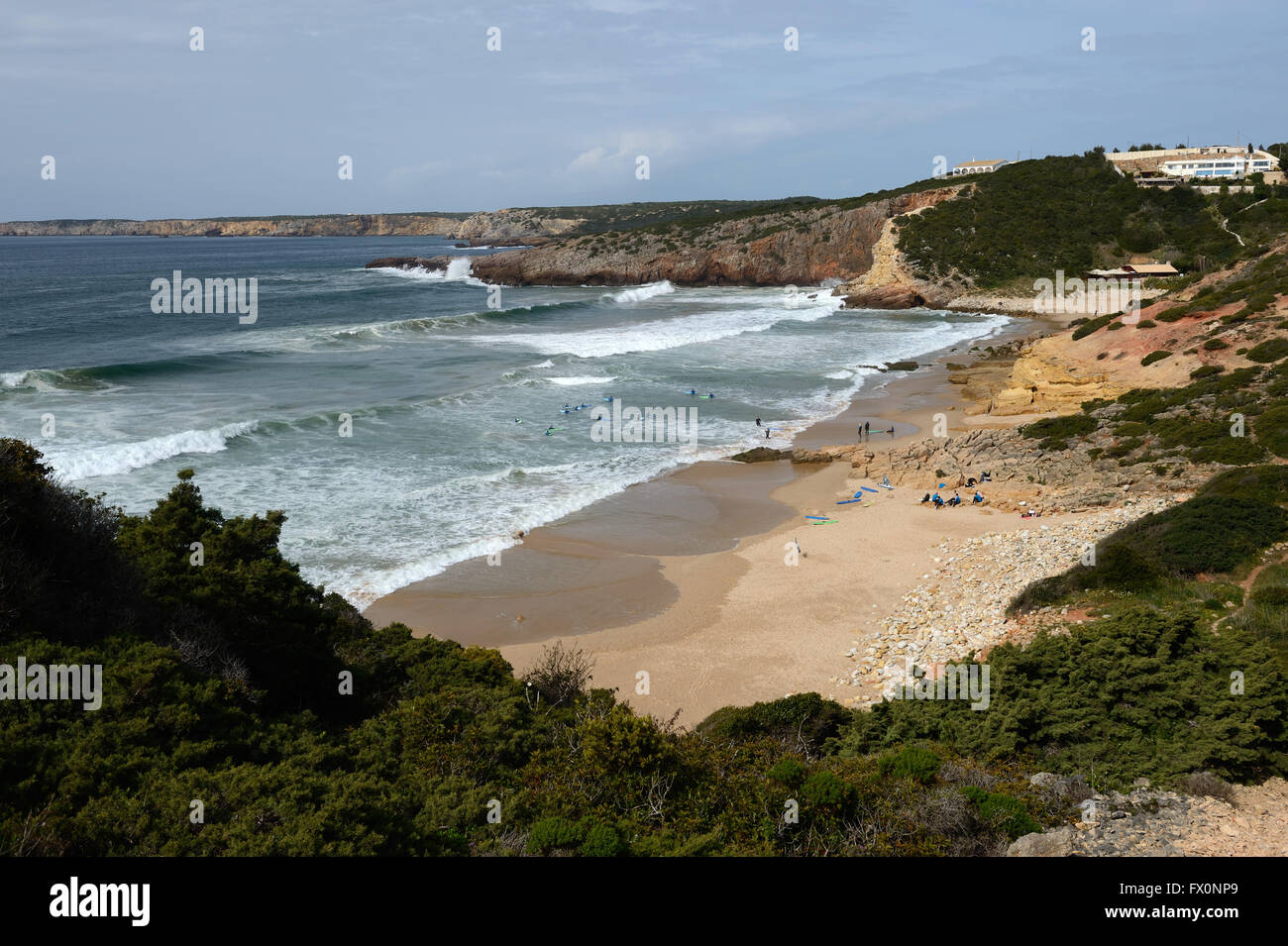 Atlantic surf rolls into a bay on the Algarve near Sagres in Portugal. A surf school practices in the shallows. Stock Photo