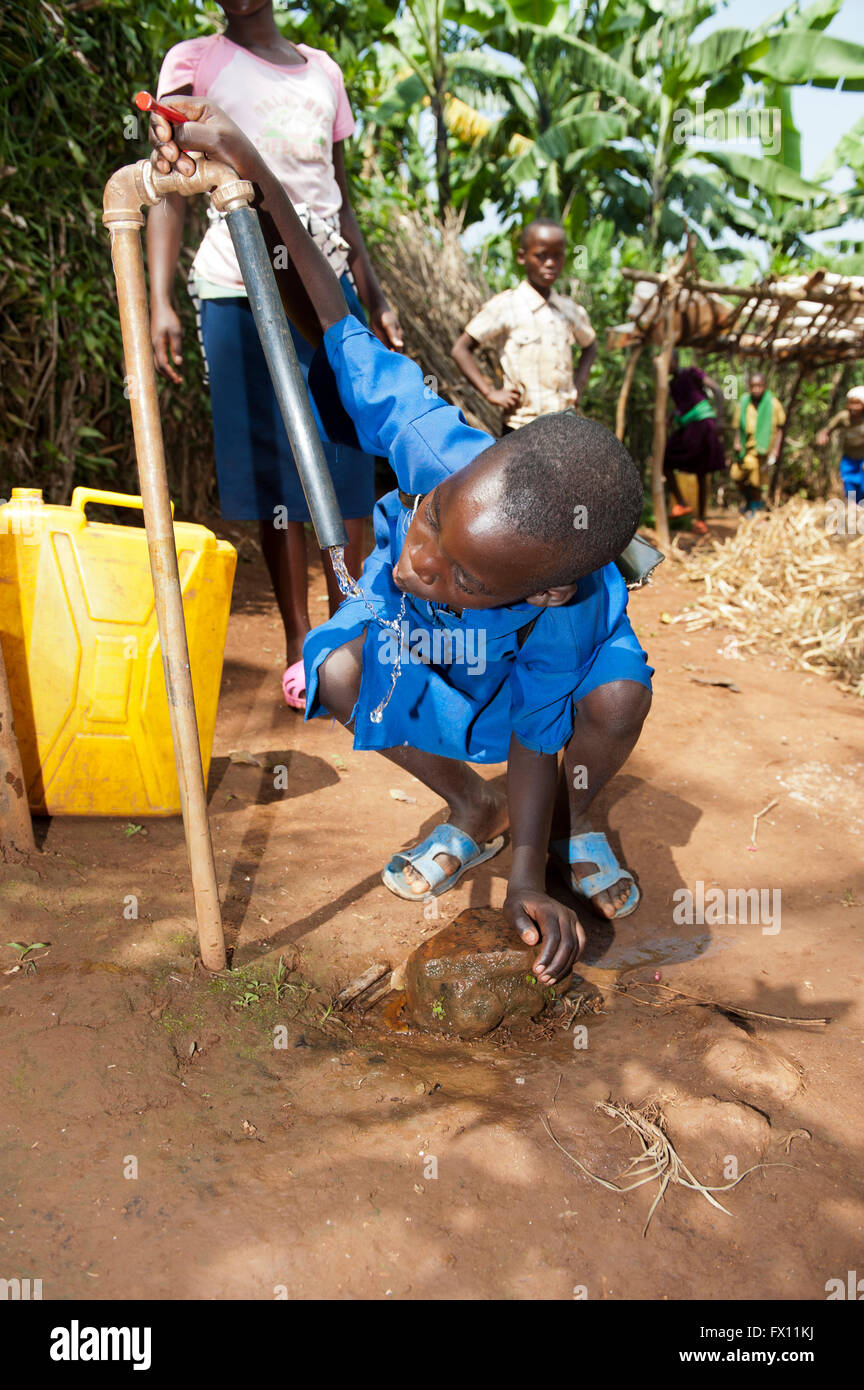 Rwandan girl drinking clean fresh water from a stand tap in the yard ...