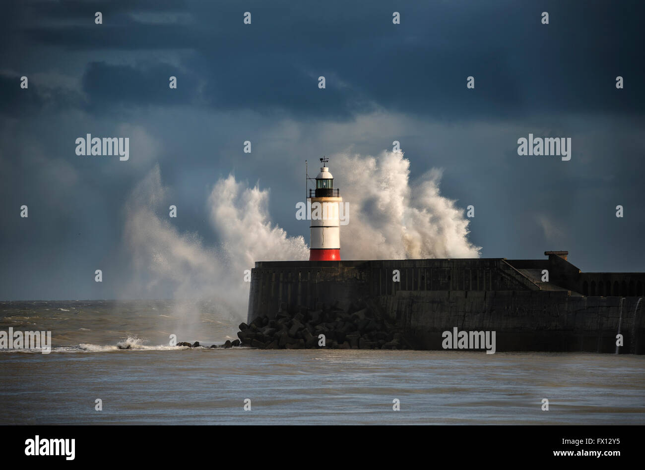 Huge sea waves crashing over lighthouse during storm with beautiful sunset light Stock Photo
