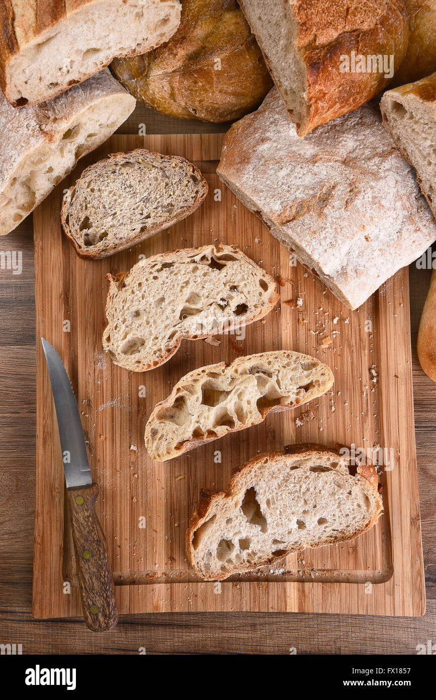 A variety of fresh baked loaves of bread, with slices on a wood cutting board. Top view in Vertical format. Stock Photo