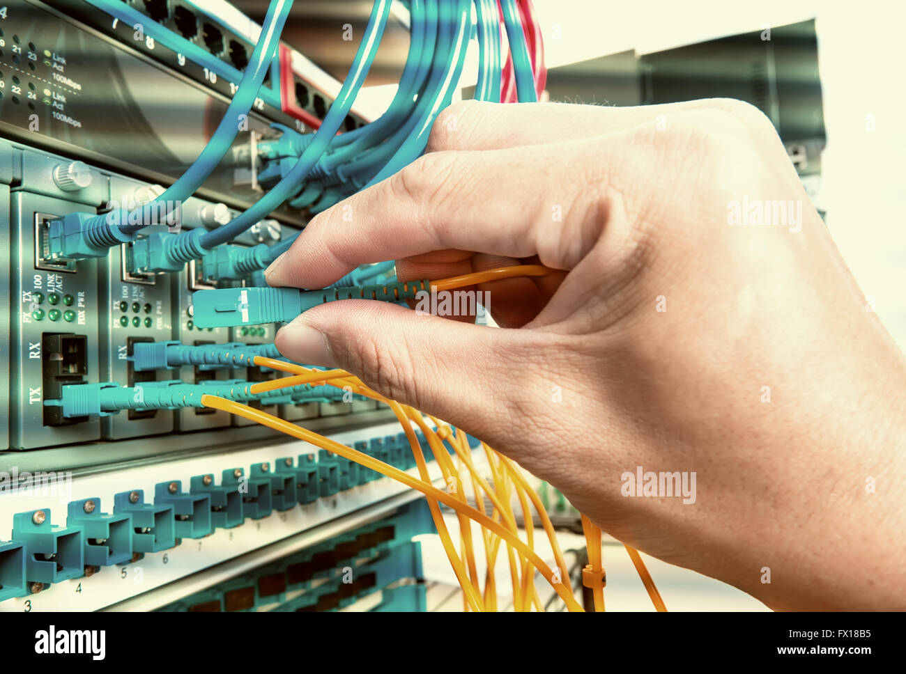 hand with fiber network cables connected to servers in a datacenter Stock Photo
