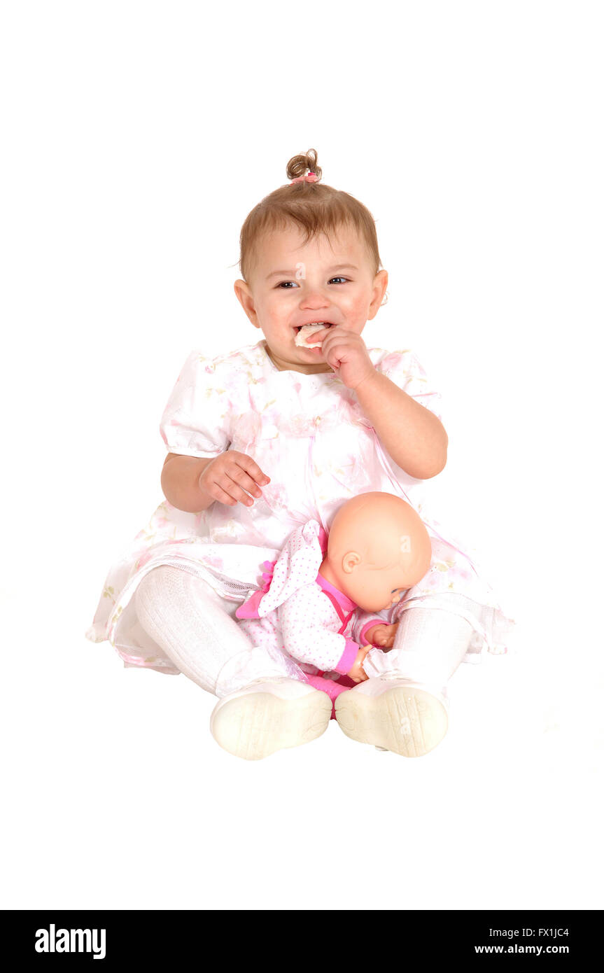 A beautiful baby in a pink dress sitting on the floor, eating a ...