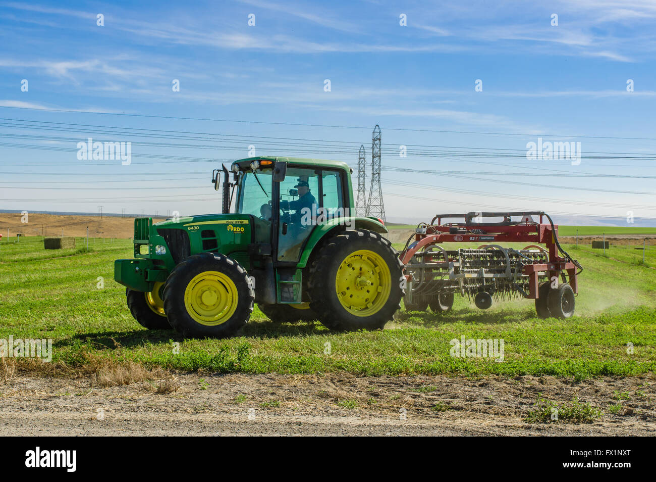 Farmer driving a tractor an rake to prepare alfalfa hay for baling.  Eastern Washington Stock Photo