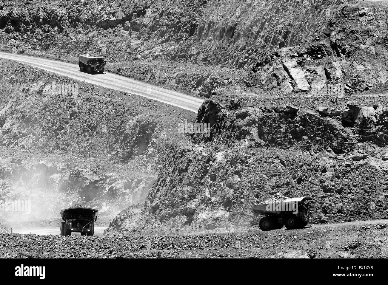 Loaded industrial trucks carrying heavy load of golden ore uphill from open pit gold mine in Kalgoorlie, Western Australia. Stock Photo