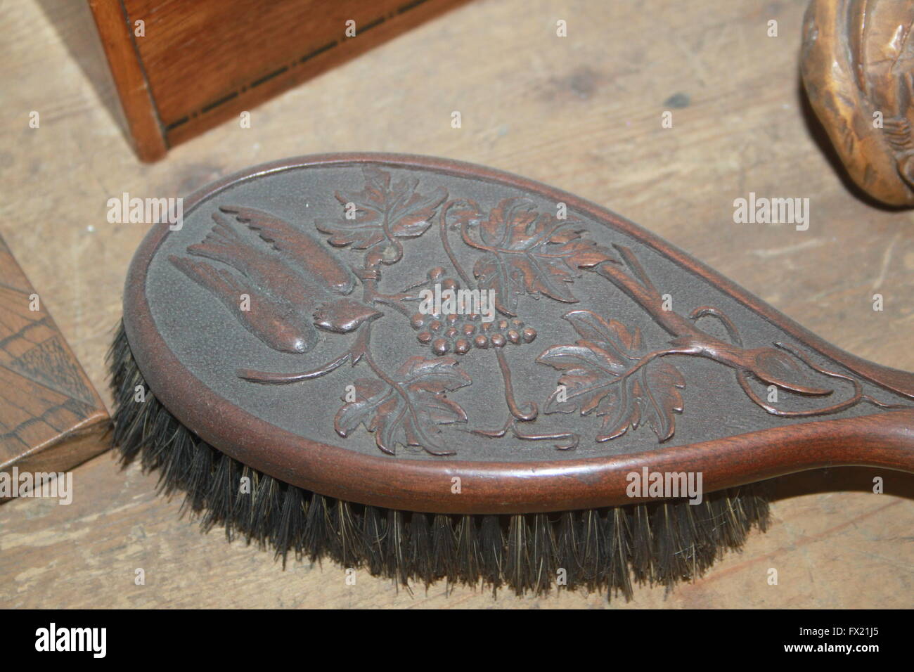 Close up of the carved bird and grape vine design in the back of an old wooden hair brush sat on a simple wooden board. Stock Photo