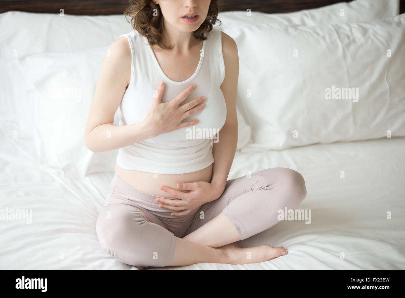 Close-up view of pregnant young woman doing yoga exercise. Female model sitting on the bed cross-legged in Easy Pose Stock Photo