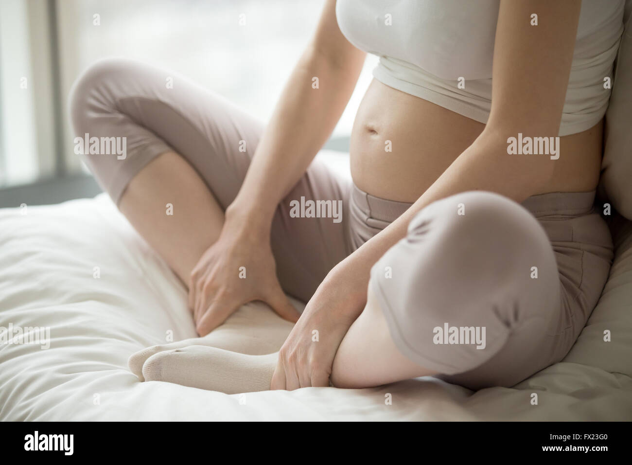 Close-up view of young pregnant woman doing morning prenatal yoga after waking up. Female model sitting in Baddha Konasana Stock Photo