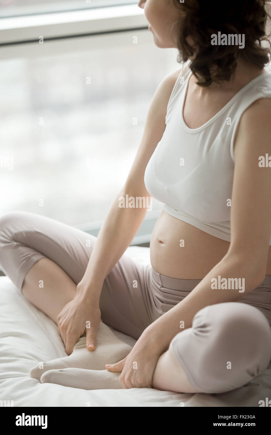 Close-up view of young pregnant woman doing morning prenatal yoga after waking up. Happy female model sitting in Baddha Konasana Stock Photo