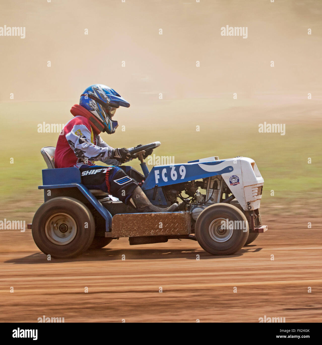 Man with colourful clothing & helmet driving blue motor mower on dusty track in unusual Australian motor racing sport Stock Photo