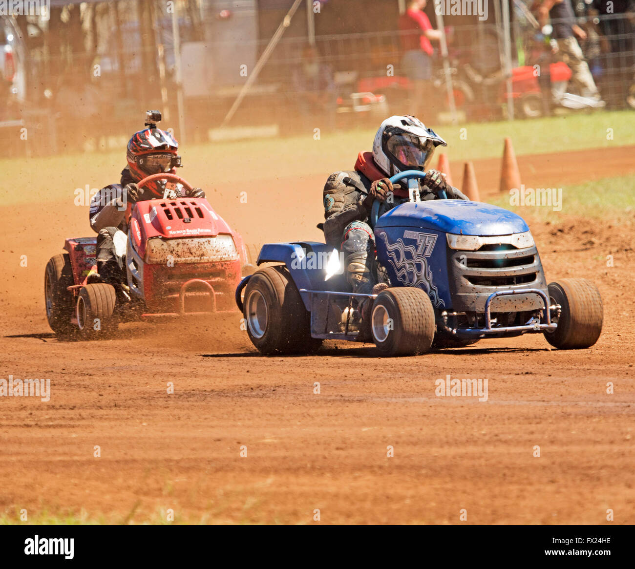 Two men with helmets &safety clothing driving ride-on mowers on dusty track competing in unusual Australian motor racing sport Stock Photo