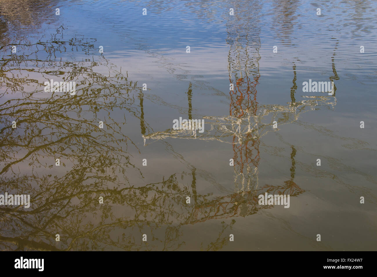 Surface of the water in the lake with small waves, reflecting the electricity tower, sky and twigs of a tree. Stock Photo