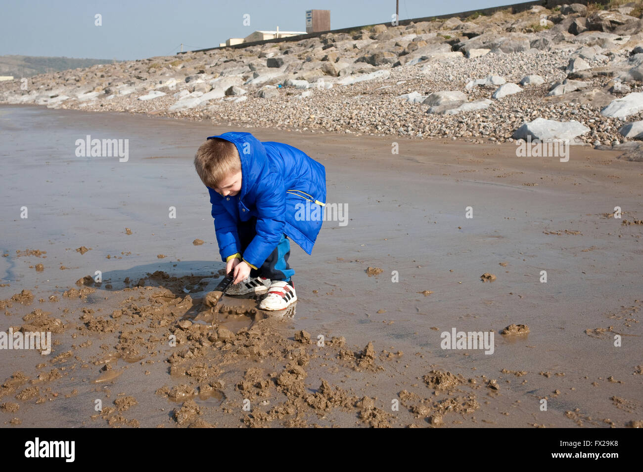young boy playing in the packed sand on the beach using an ad hoc spade Stock Photo