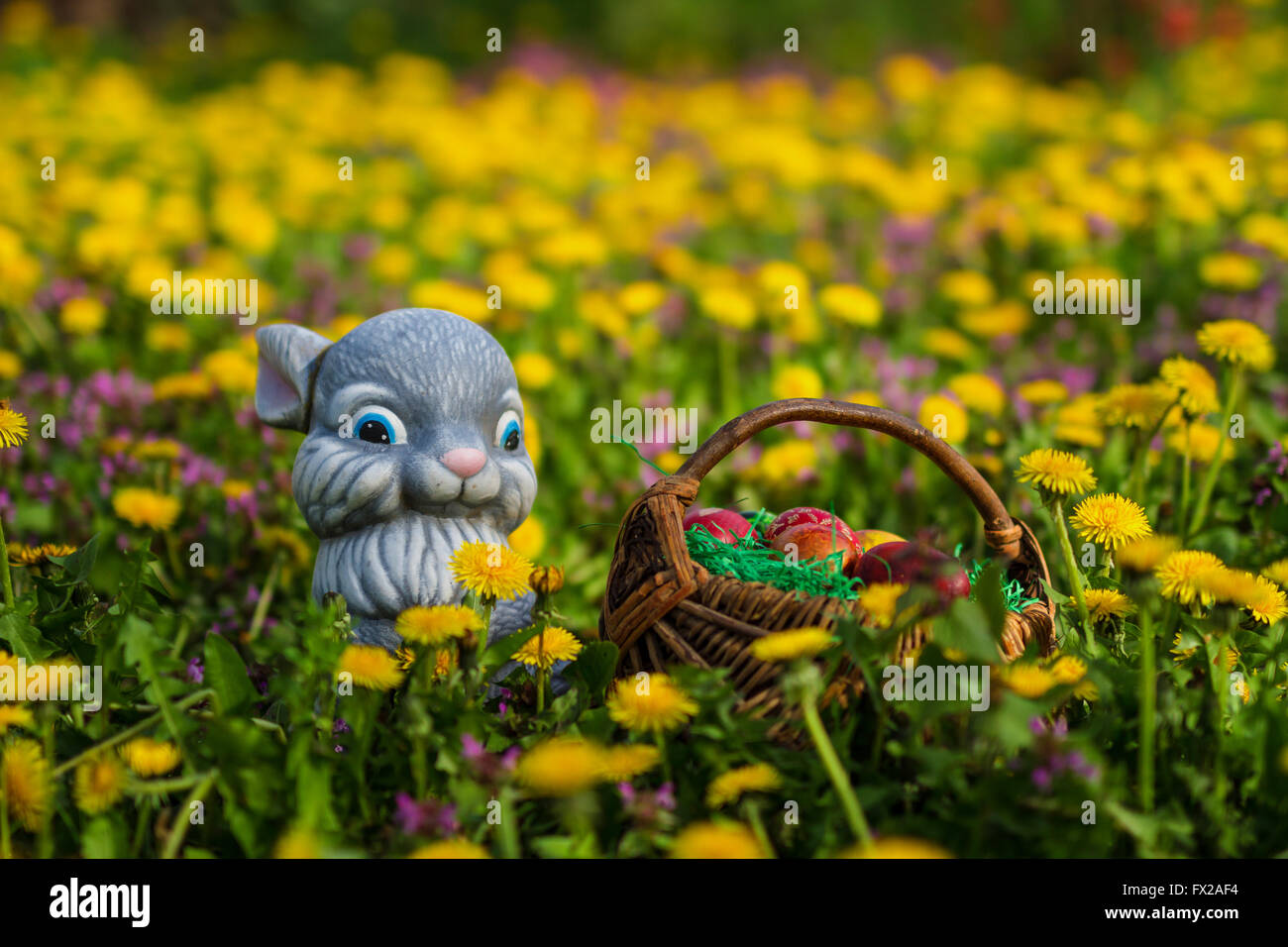 Easter eggs in basket with rabbit on green grass meadow with flowers Stock Photo