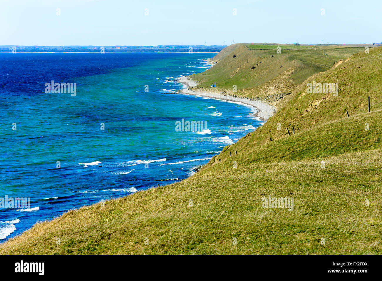 Grass covered coastal hills in spring. Weather is sunny and calm. Small house on the beach gives scale. Kaseberga coastline in S Stock Photo