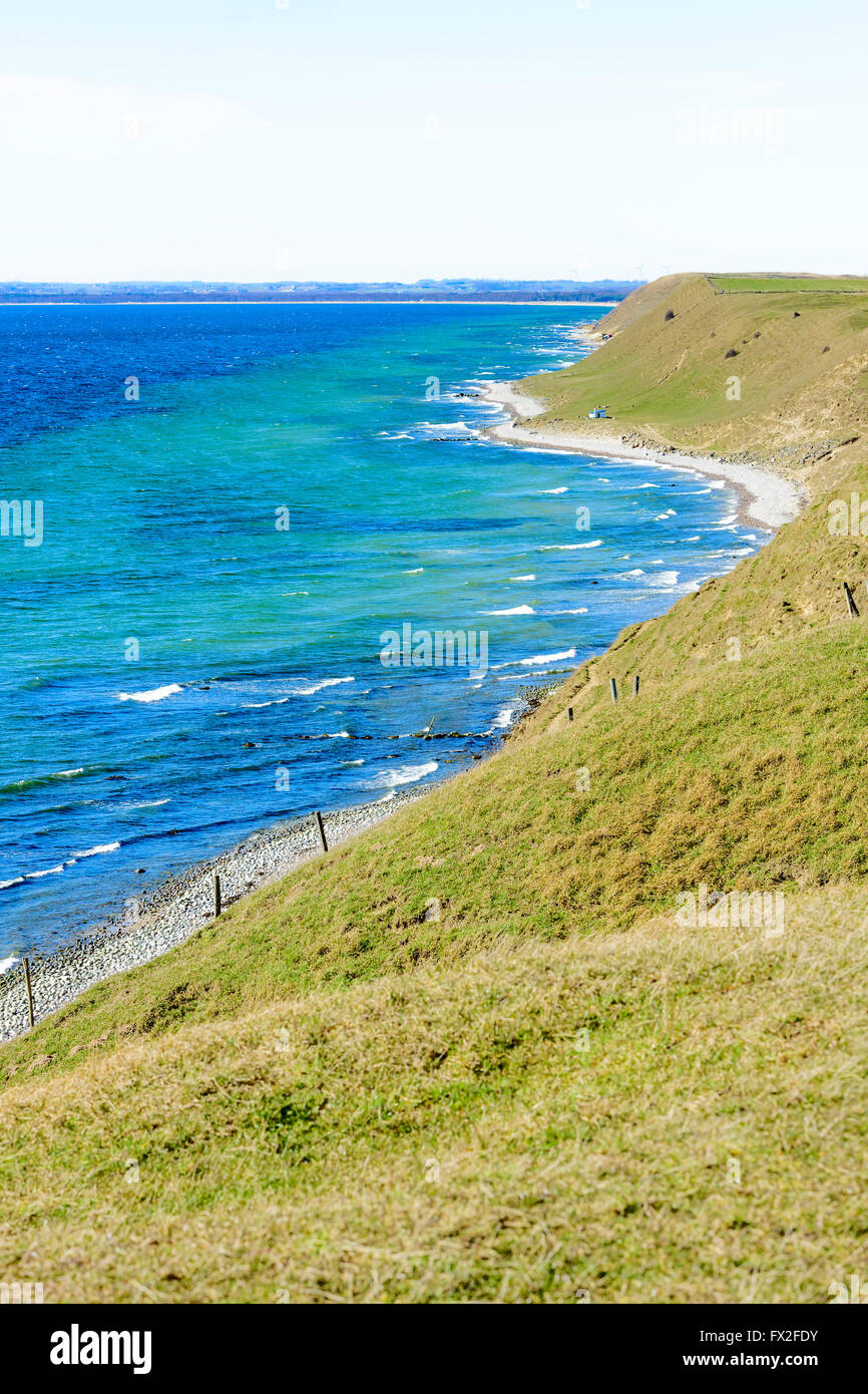 Grass covered coastal hills in spring. Weather is sunny and calm. Small house on the beach gives scale. Kaseberga coastline in S Stock Photo