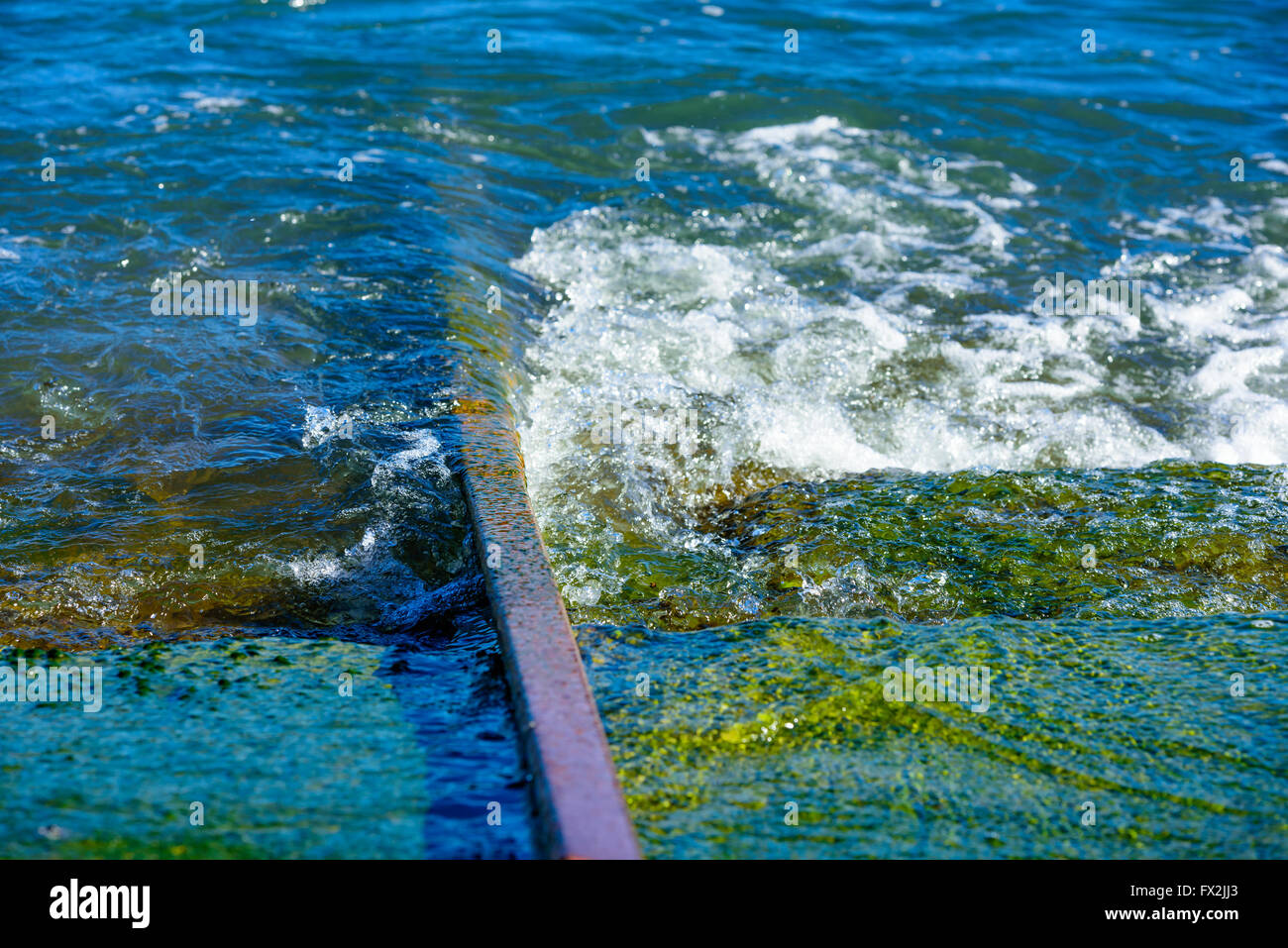 Seawater swirling around an iron rail leading into the sea. Rail is for launching boats in the marina. Green algae growth by the Stock Photo