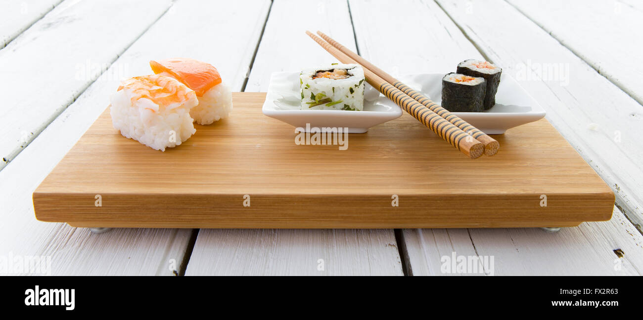 Sushi served on a Bamboo board with chopsticks on a rustic white wooden board Stock Photo