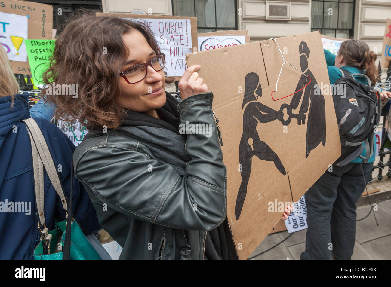 London, UK. 9th April, 2016. A woman holds a poster with a wire coat hanger, the traditional crude tool of back-street abortionists, on it ooutside the Polish embassy. The poster shows a woman wrestling a key from a Catholic bishop. The London protest followed large protests in Poland against the bill proposed by the Law and Justice Party (PiS) which will outlaw abortion in all cases, protecting the life of the unborn child even where this may cause extreme distress or even death for the mother. Peter Marshall/Alamy Live News Stock Photo