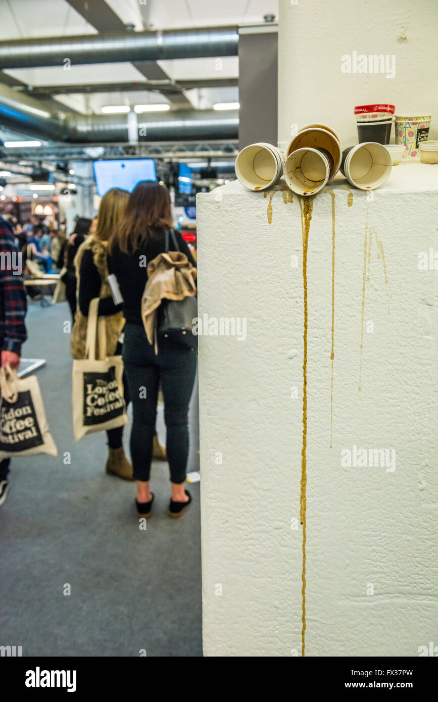 London, United Kingdom - April 09, 2016: The London Coffee Festival (07-10 April, Brick Lane, Old Truman Brewery). Lots of empty mugs left after coffee tasting. Girls with tote bags with the festival logo standing in the background Stock Photo