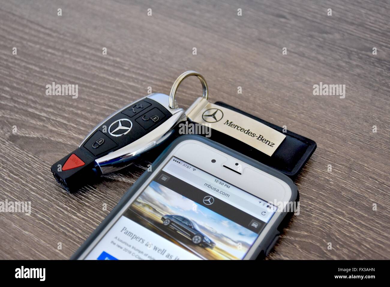 An Apple iPhone displaying the Mercedes-Benz web page while laying next to a Mercedes-Benz key fob Stock Photo