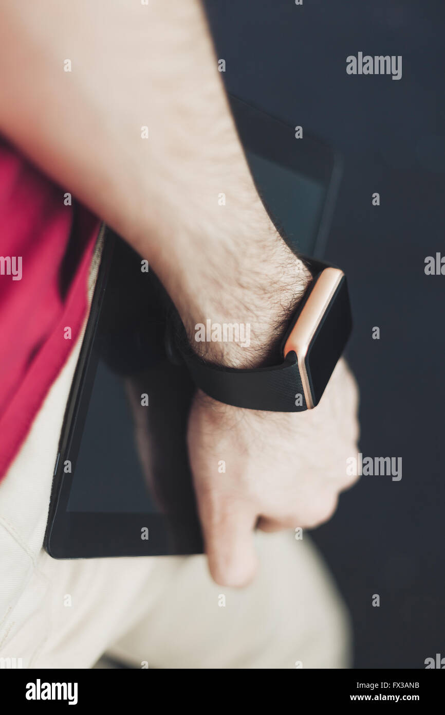 Male hand holding smart wrist watch and tablet pc. Modern stylish gadgets to be always connected. Vertical orientation, fading colors Stock Photo