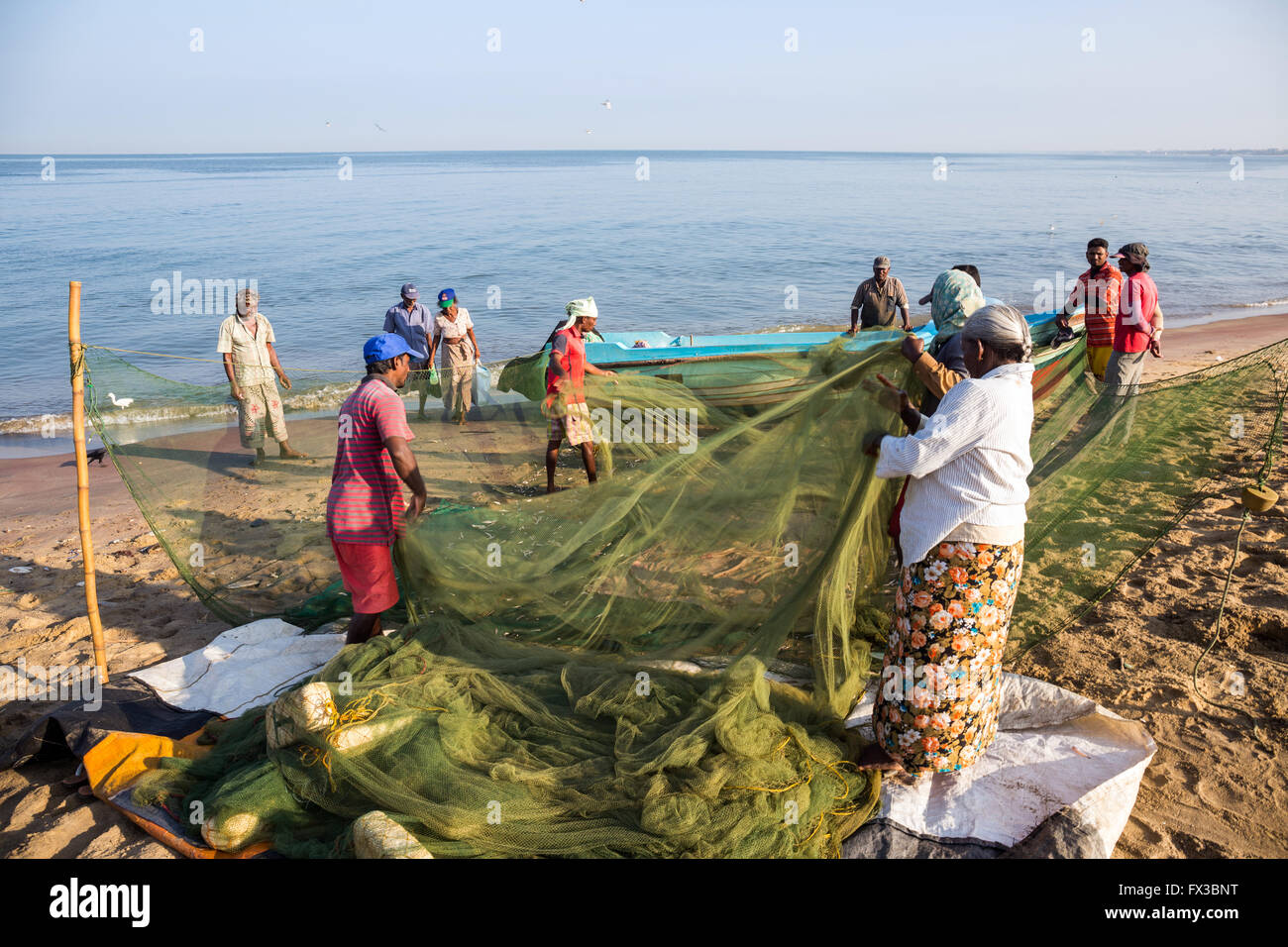 People repairing fishing nets amidst their colorful fishing boats at