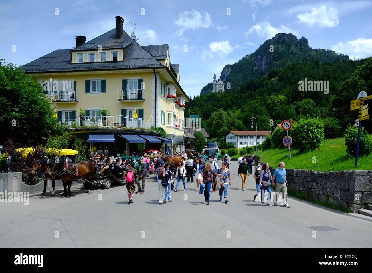 Tourists in the Bavarian village of Hohenschwangau, near Füssen in Germany, with Neuschwanstein Castle on the hill beyond. Stock Photo