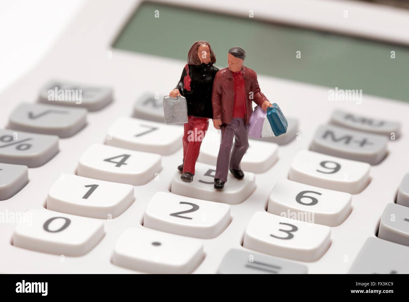 Miniature figurine shoppers carrying bags across a calculator key pad. Stock Photo