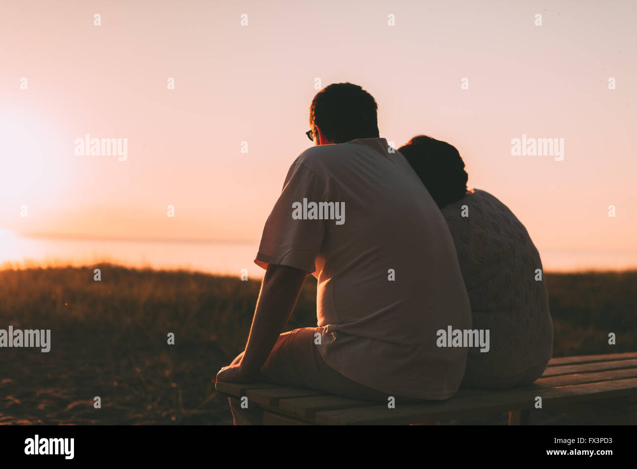 Side view a married couple a silhouette sitting on a bench. Stock Photo