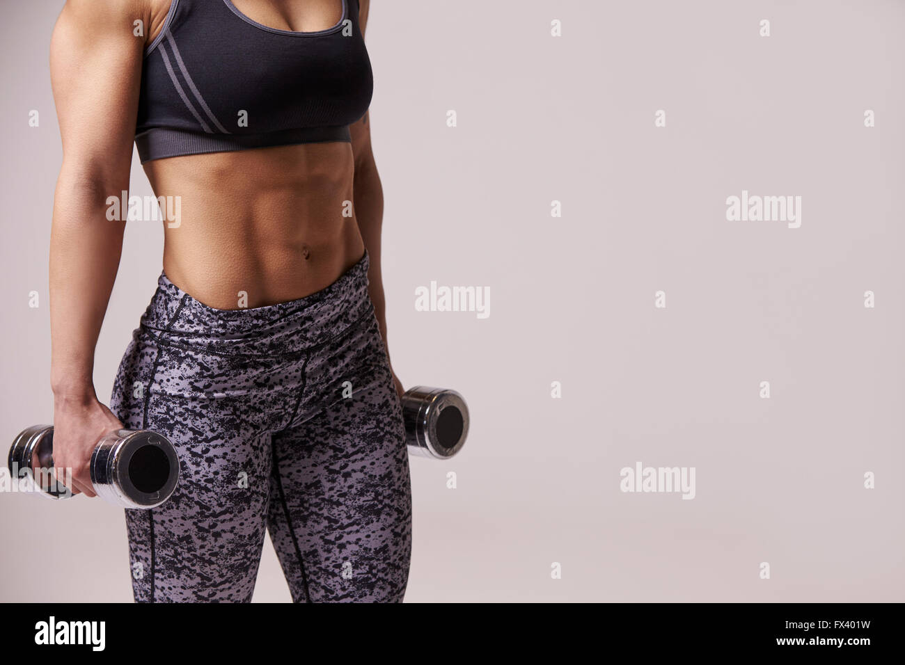 Dark haired young woman using dumbbells, mid section crop Stock Photo