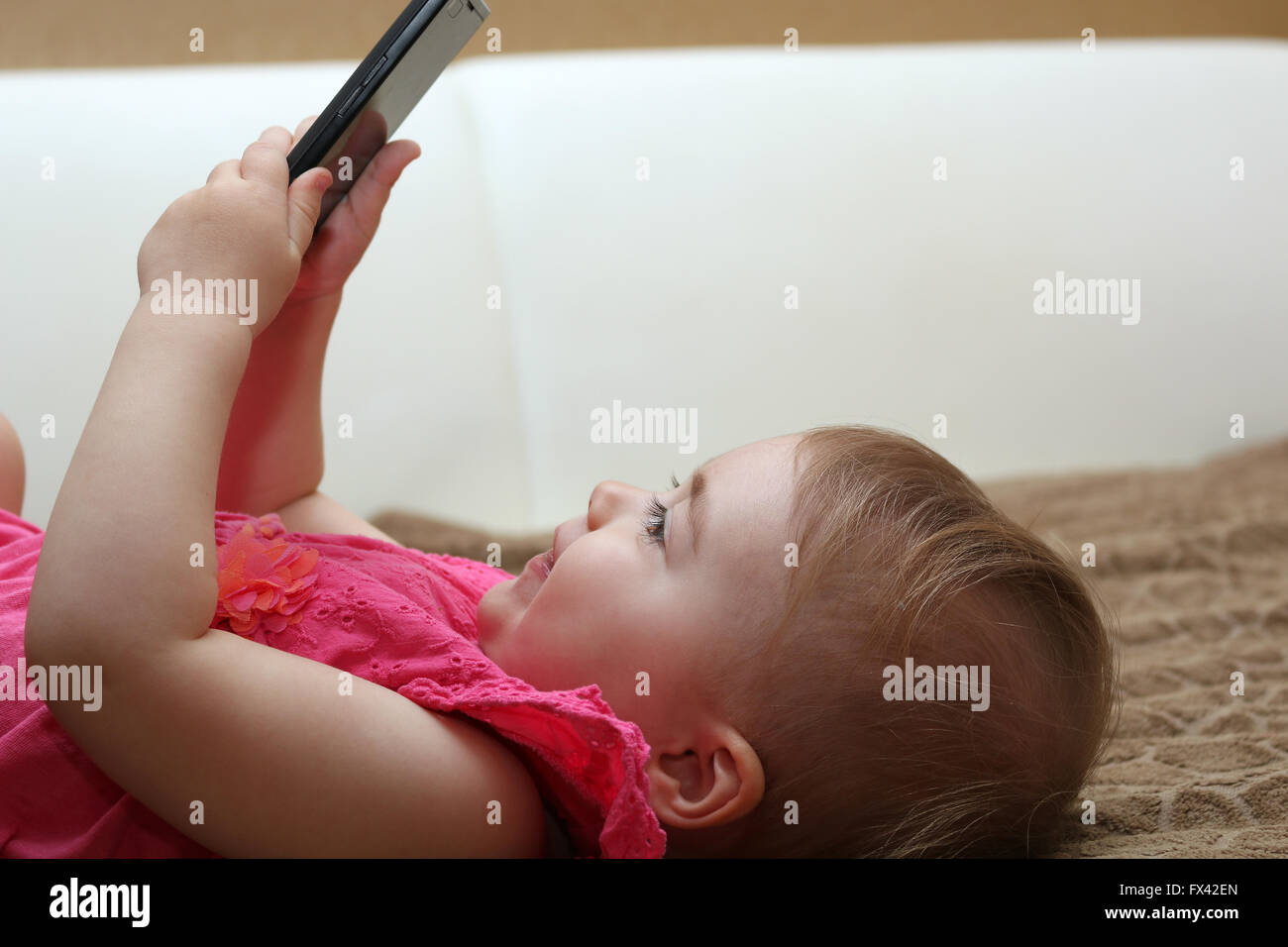 little cute girl lying on the couch and playing with a smartphone Stock Photo