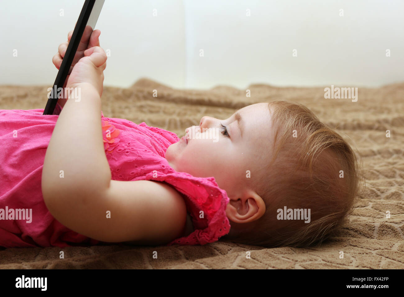 little cute girl lying on the couch and playing with a smartphone Stock Photo