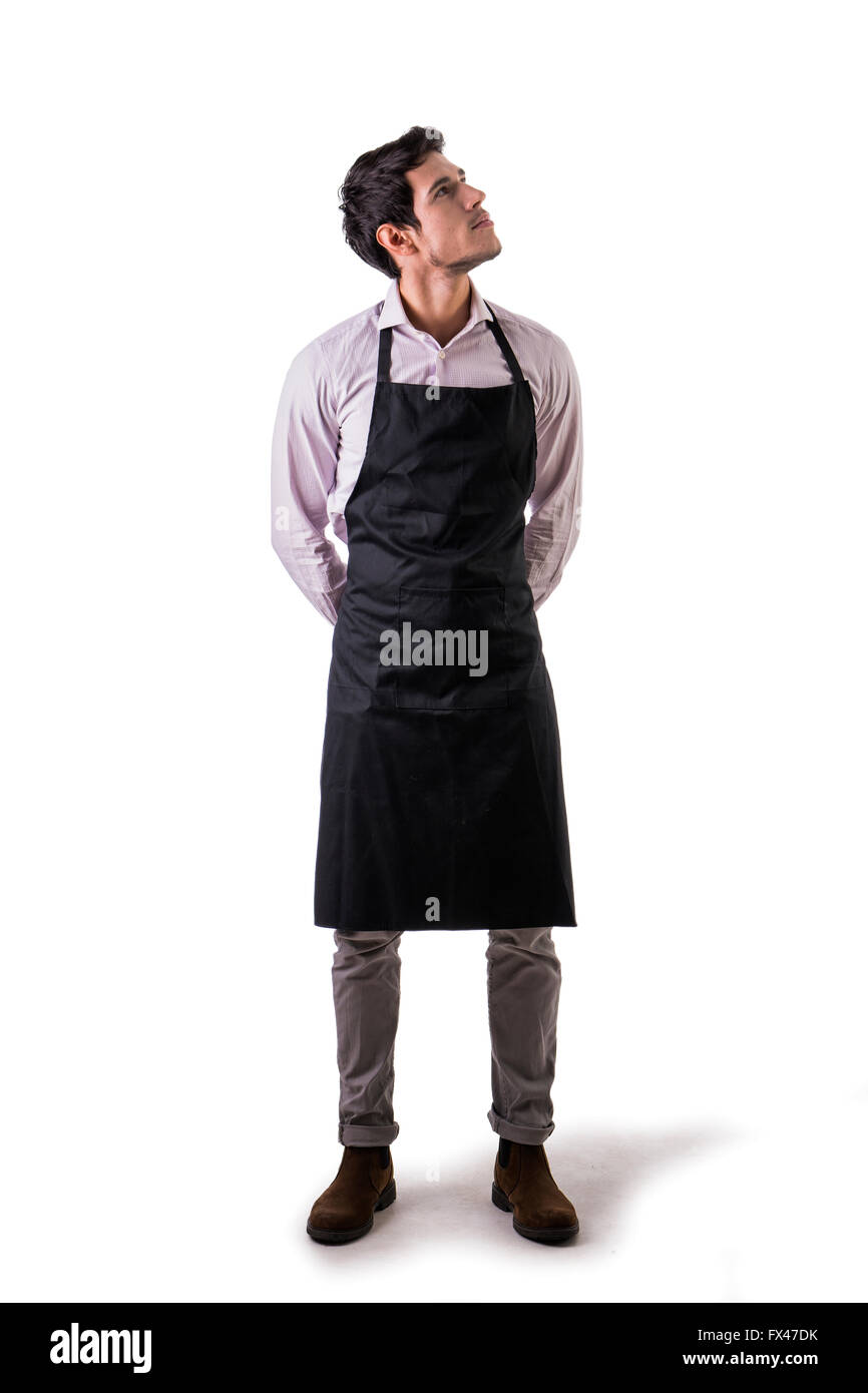 Young chef or waiter posing, wearing black apron and shirt isolated on white background, looking up to a side Stock Photo