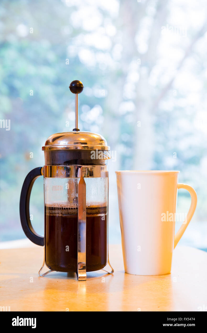 Coffee is being made in a french press along with cream and sugar on the kitchen counter early in the morning. Stock Photo