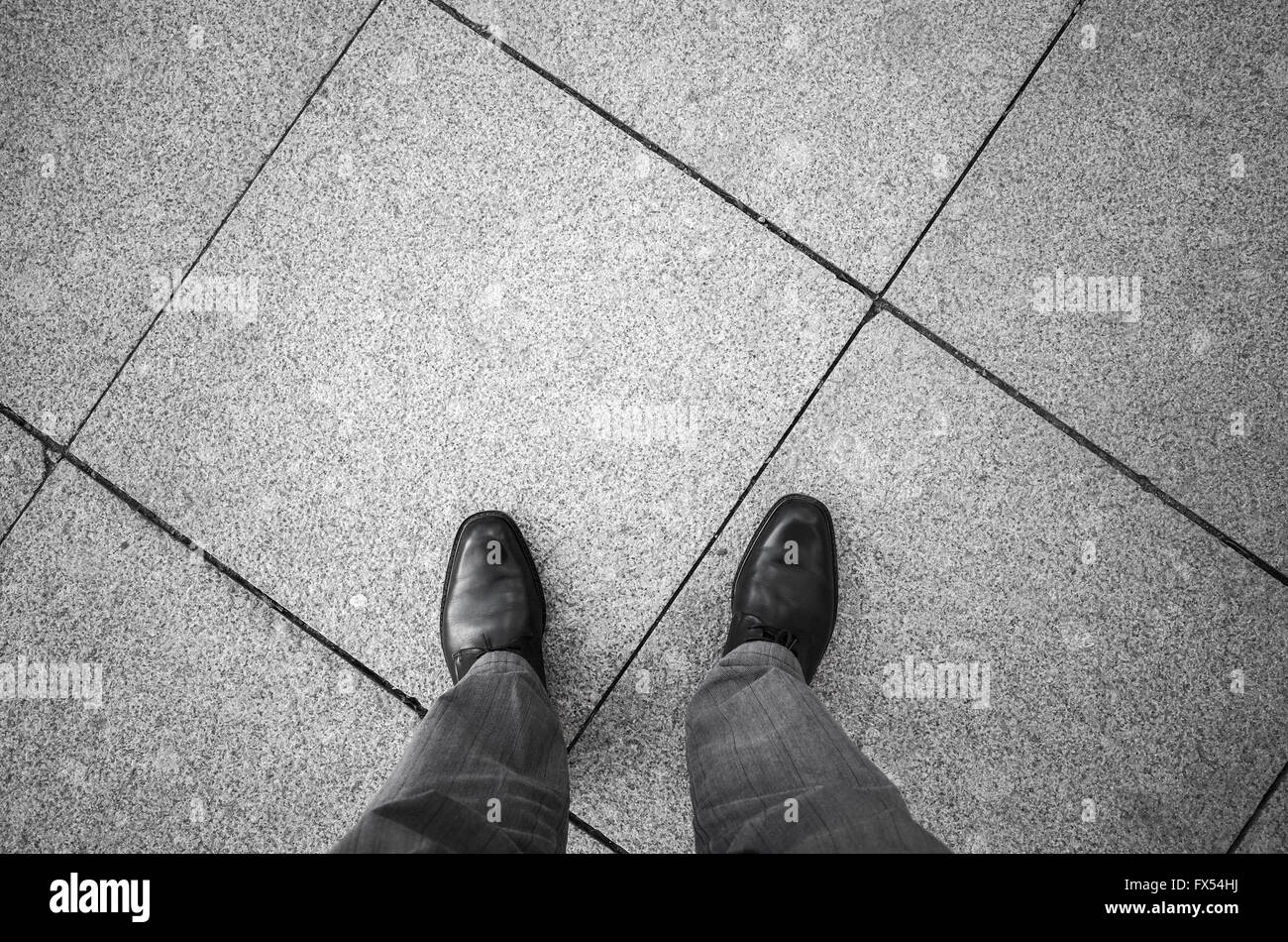 Feet of an urbanite man in black new shining shoes standing on gray cobblestone tiling Stock Photo