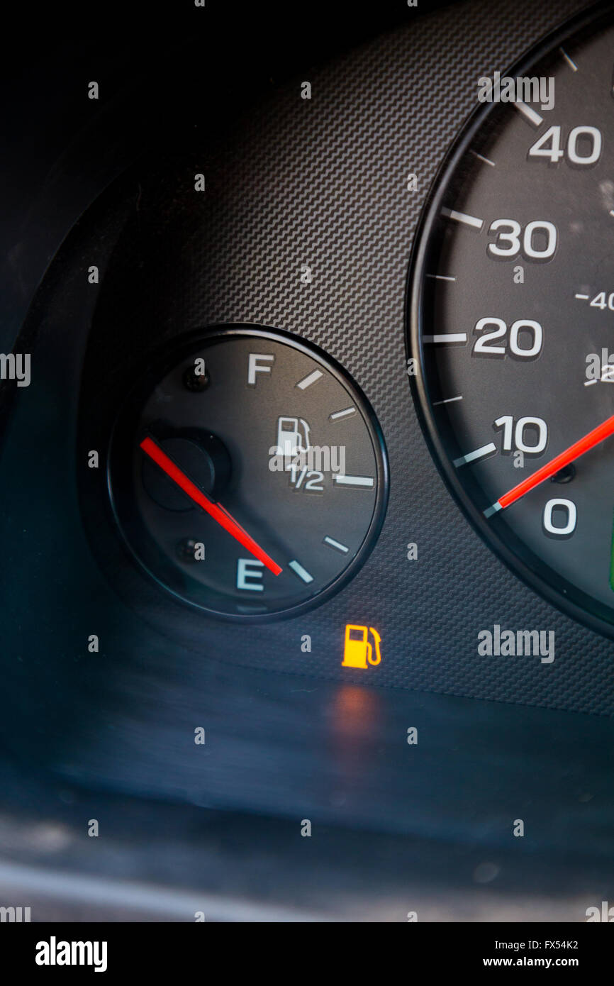 A gas guage in a car reads empty and shows the warning light to let the driver know they are out of gas and need to refuel. Stock Photo