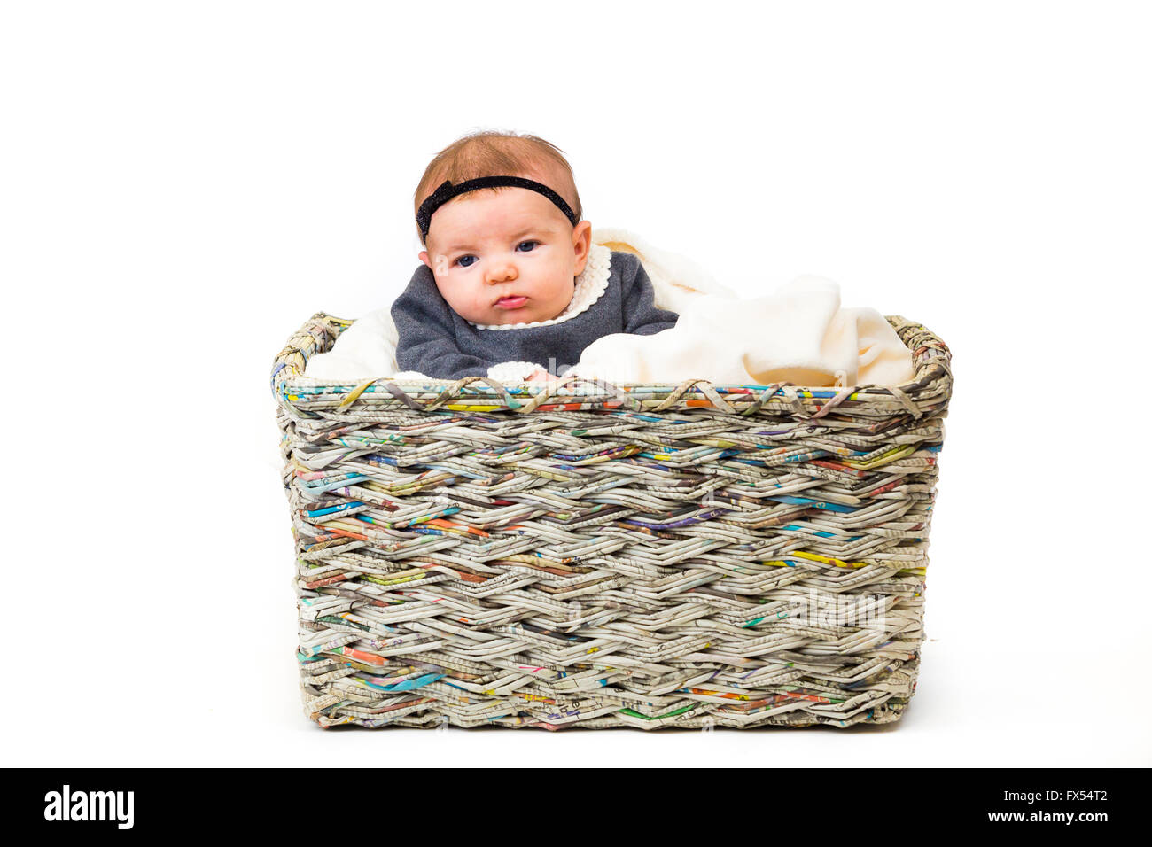 Young newborn baby wearing a cute outfit posing for portraits in the studio with a white background sitting inside a basket with Stock Photo
