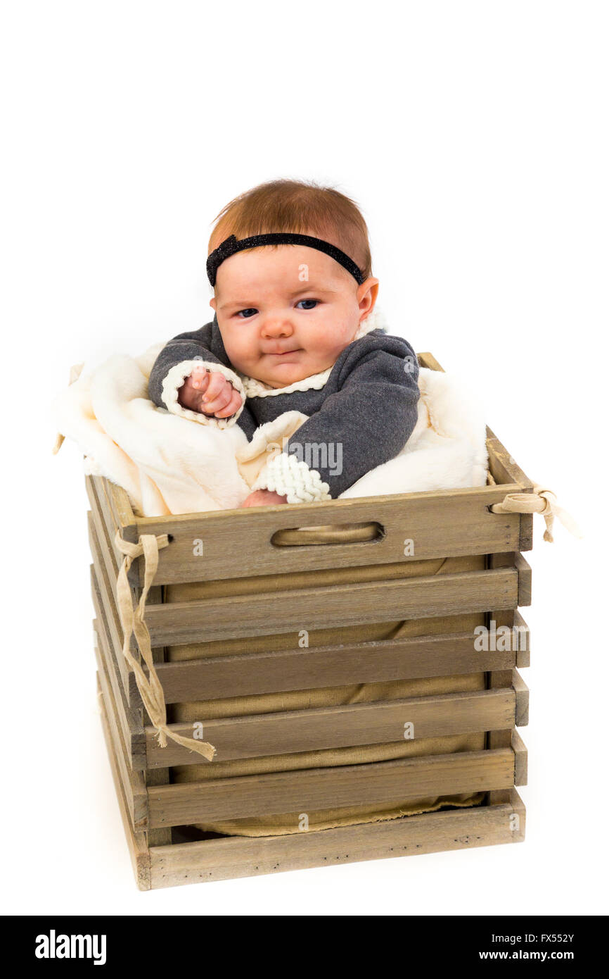 Young newborn baby wearing a cute outfit posing for portraits in the studio with a white background sitting inside a basket with Stock Photo