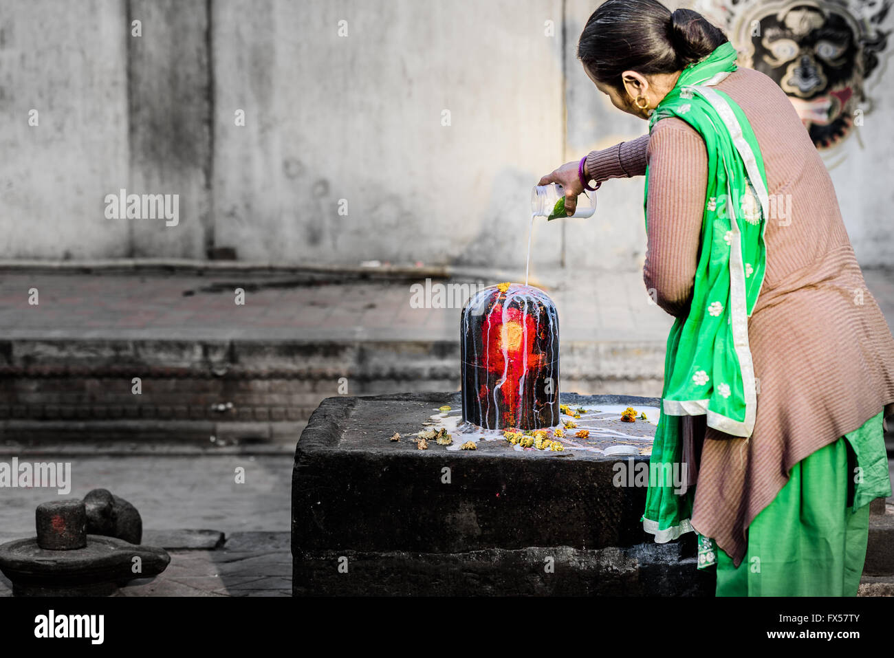 A female devotee pouring milk in Shiva Lingam in a Hindu temple in Nepal Stock Photo
