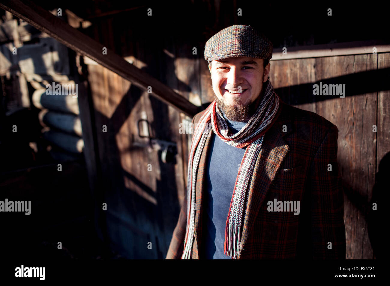 Man in flat cap with old-fashioned outfit outdoors on  background of wooden constructions. Stock Photo