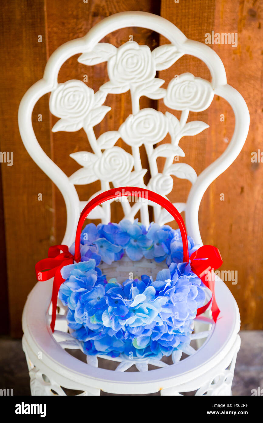 Flower girl basket on a white chair with flowers in it ready for a wedding ceremony. Stock Photo