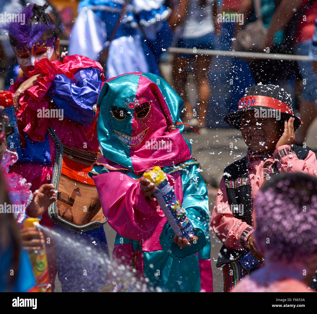 People getting sprayed with foam by masked children at the annual Carnaval Andino con la Fuerza del Sol in Arica, Chile. Stock Photo