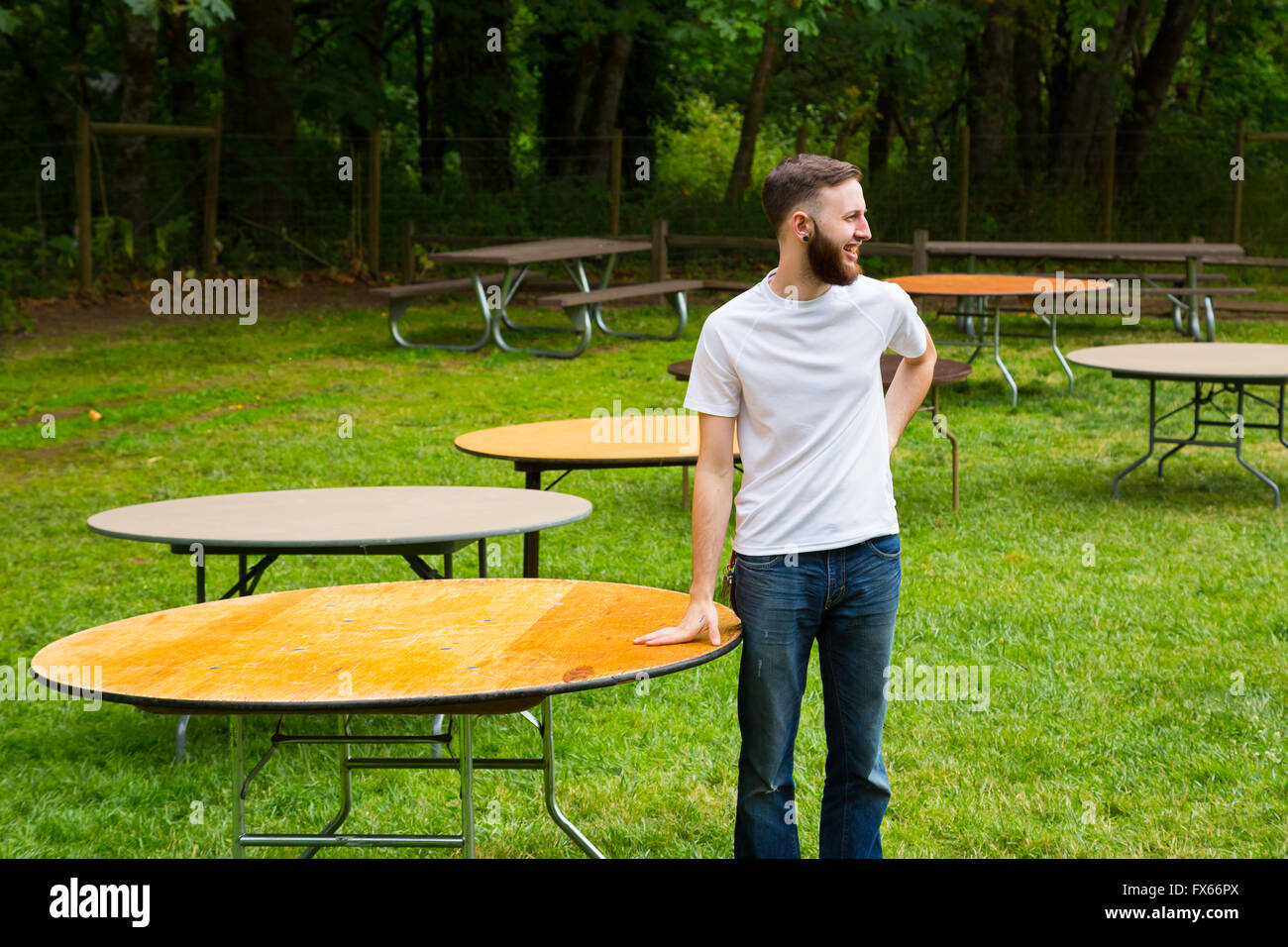 Groom wearing a white t-shirt setting up tables on his wedding day outdoors. Stock Photo
