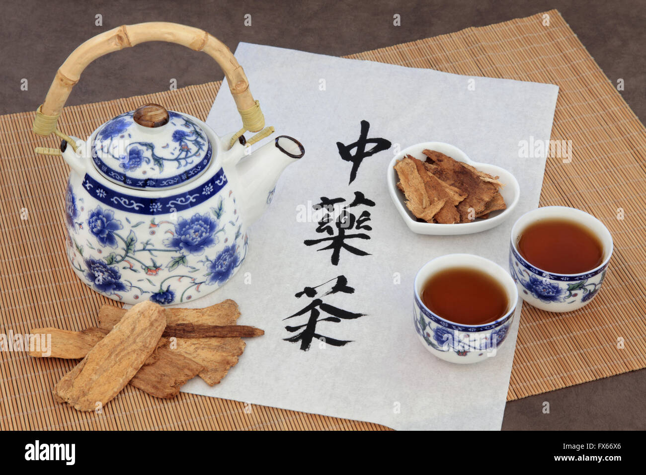 Astragalus herb tea also used in chinese herbal medicine, with cups and calligraphy script on rice paper over bamboo. Stock Photo