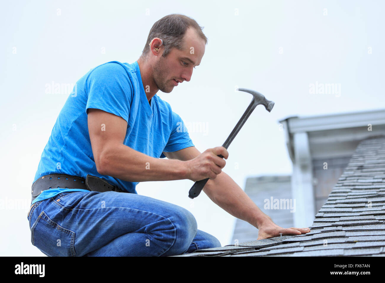 Deaf Caucasian roofer hammering on roof Stock Photo