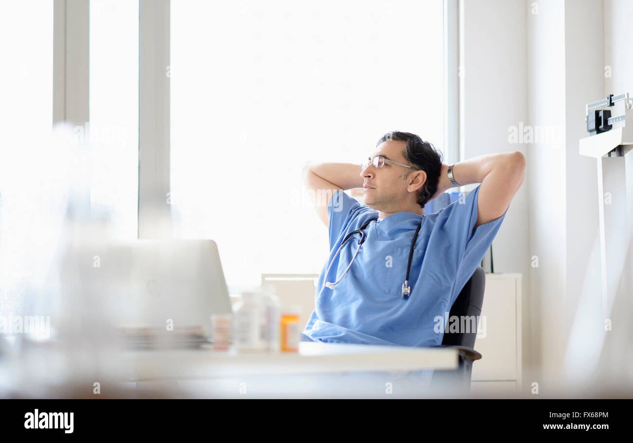 Mixed race doctor relaxing at desk Stock Photo